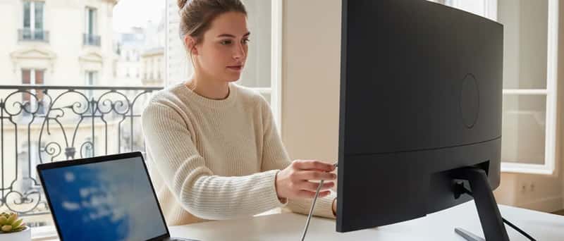 Femme connectant un câble USB-C entre un ordinateur portable et un écran moniteur sur un bureau minimaliste