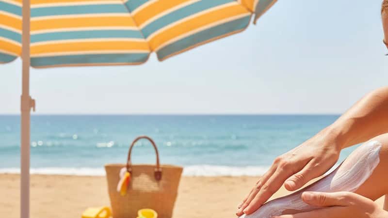 Des mains appliquant de la crème solaire sur le bras d'un enfant sous un parasol de plage à Marseille