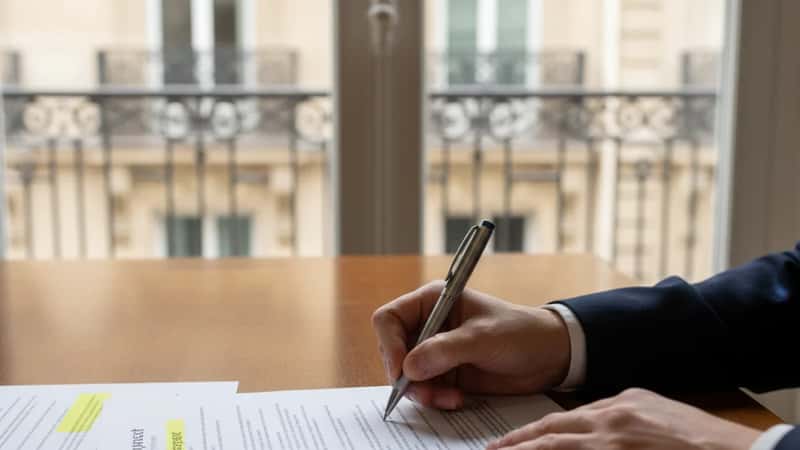 Hands signing an employment non-compete contract in an Indianapolis office with highlighted clauses visible