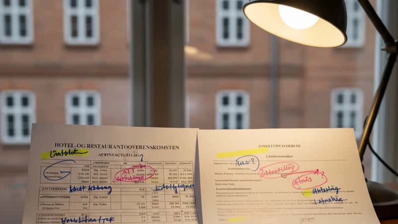 To overenskomstdokumenter sammenlignes side om side på et konferencebord i Aarhus