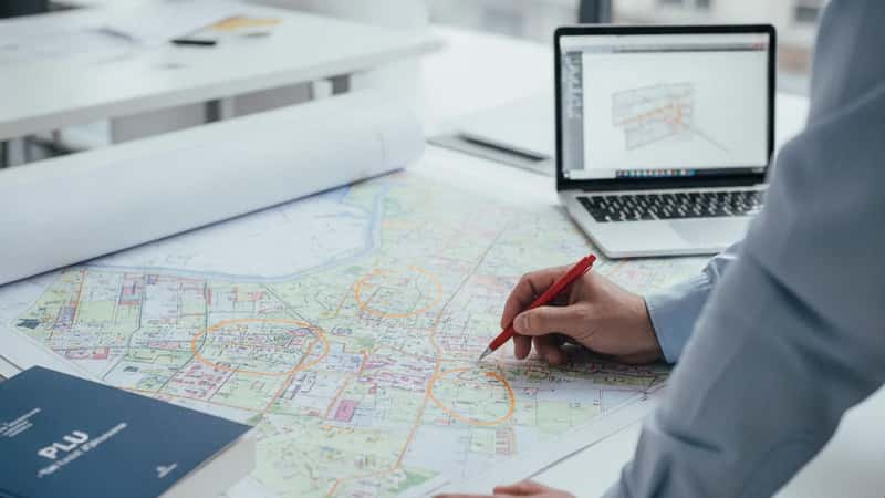 Mains pointant vers une carte PLU dans un bureau d'urbanisme à Montpellier, parcelles en zone agricole surlignées