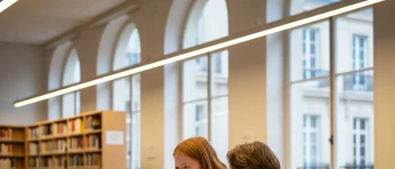 To norske tenåringer studerer sammen ved et bibliotekbord med bærbare datamaskiner