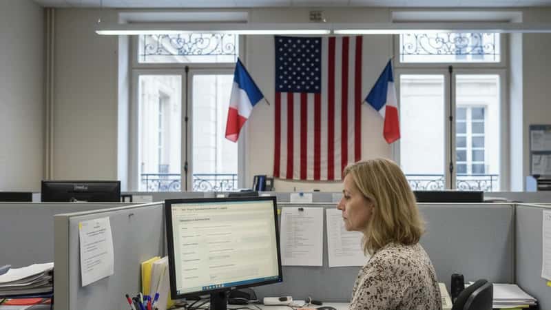 Woman filing a wage complaint online at a New York State Department of Labor regional office, fluorescent lighting, American flag in background