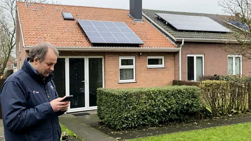 Nederlander met smartphone bij huis met zonnepanelen, controleert energieverbruik dynamisch contract