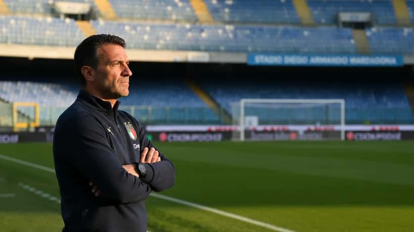 Allenatore di calcio in riflessione sul bordo campo a Napoli, luce mediterranea del pomeriggio