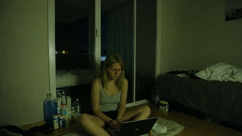 Ung norsk kvinne sitter alene i mørkt rom med laptop og viser tegn på emosjonell utmattelse