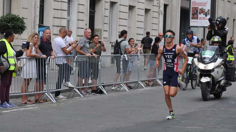 Triatleter svømmer i åpent vann under Paris 2024-testeventet, med dommere og publikum langs bredden
