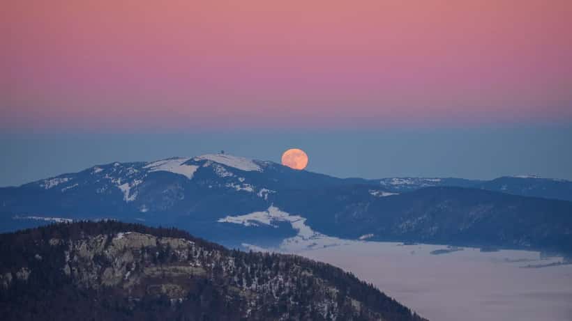 A large amber full moon rising at sunset behind the Swiss Alps, Chasseral