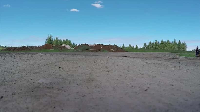 Drone flyver lavt over skov under træning med operatør i baggrunden