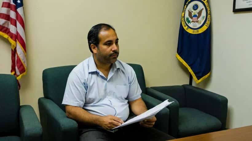 Hombre hispano en sala de espera de tribunal de inmigración consultando con su abogado en Washington D.C.