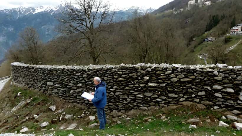 Expert en bâtiment inspectant un mur de soutènement fissuré sur une pente alpine après un glissement de terrain