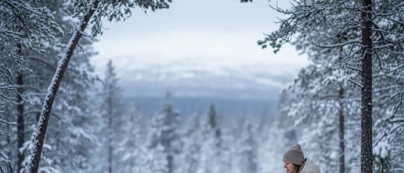 Svensk friluftsperson sitter lugnt i vinterskogen i Jämtland, reflekterande stund