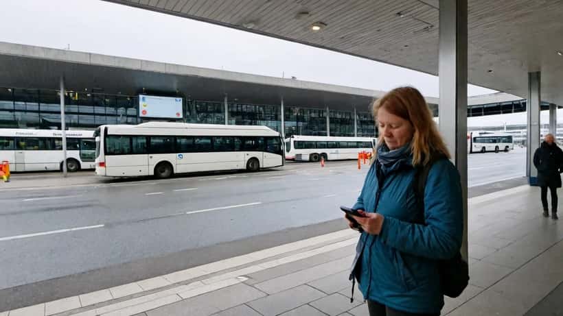 Kvinde venter ved busstoppested med turistbus i baggrunden