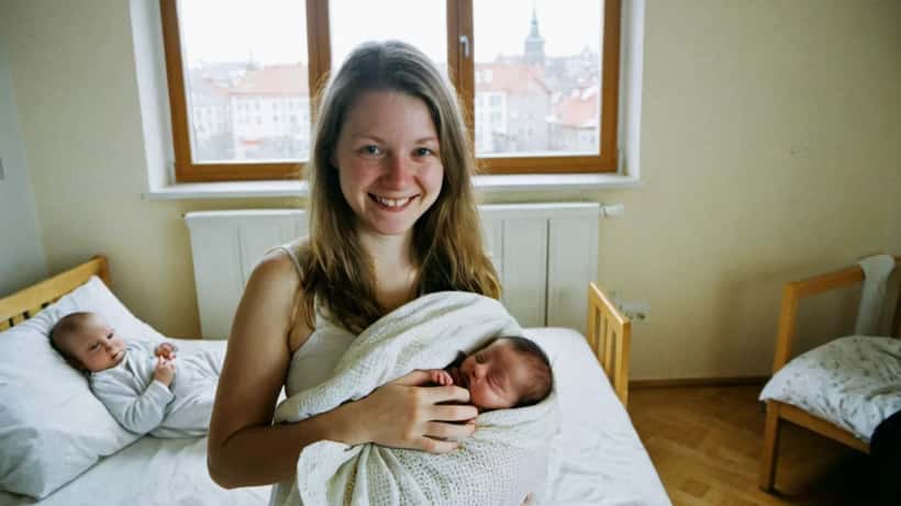 Nuori suomalainen äiti pitää vastasyntynyttä vauvaa sylissään kirkkaassa kotinsa olohuoneessa