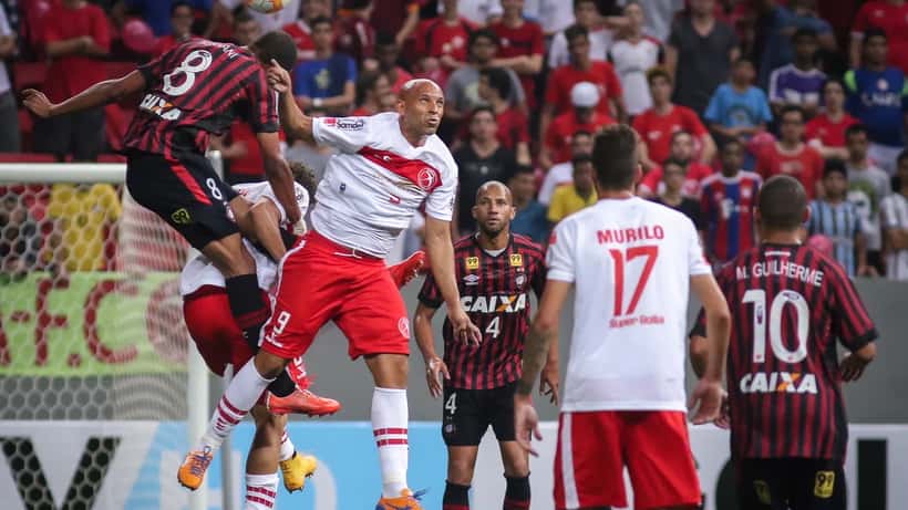 Partida de futebol no estádio com jogadores brasileiros em disputa de bola