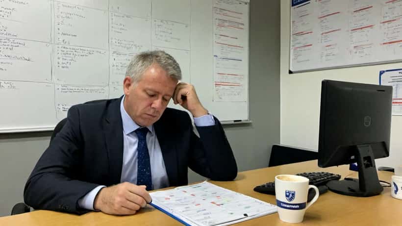 Manager aan bureau kijkt uitgeput naar rapporten in kantoor voetbalclub Alkmaar