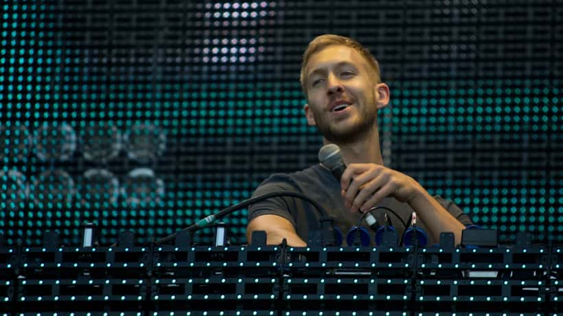 Calvin Harris performing on stage at an outdoor festival with DJ setup and large crowd