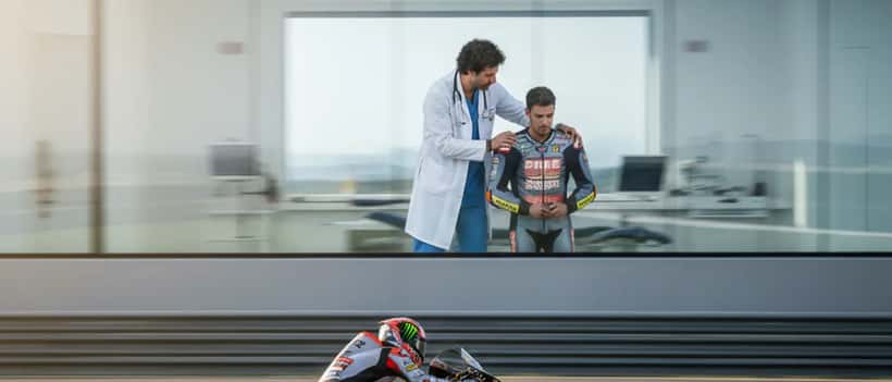 Moto da corsa in curva e medico sportivo che esamina un pilota nel box medico