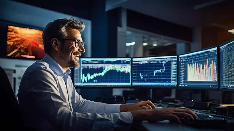Asesor financiero revisando gráficas del mercado bursátil en pantallas de ordenador