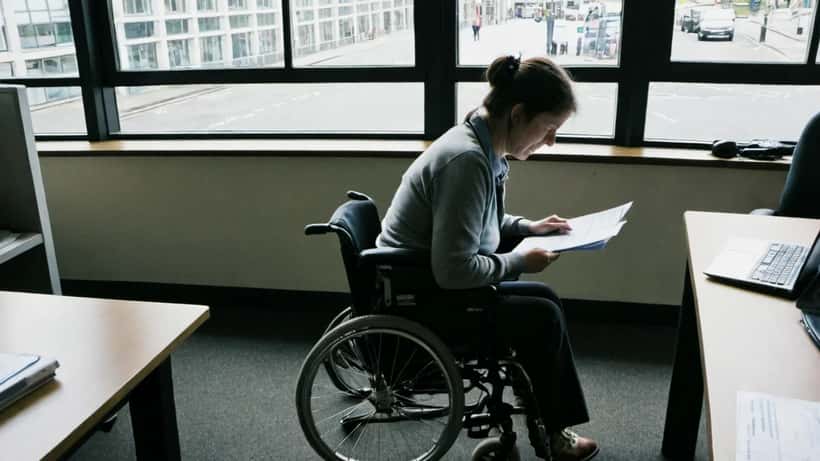 Woman in wheelchair reviewing benefit claimant paperwork at accessible office desk in London