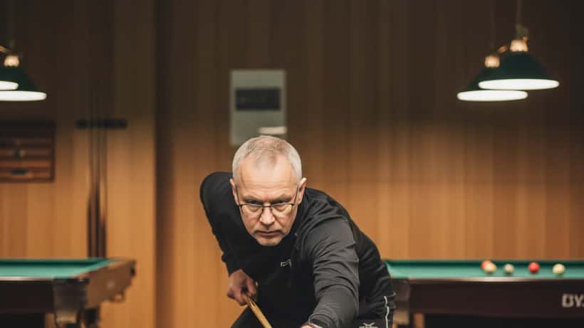 50-vuotias suomalainen mies pelaa snookeria Helsingissä, terve ja keskittynyt
