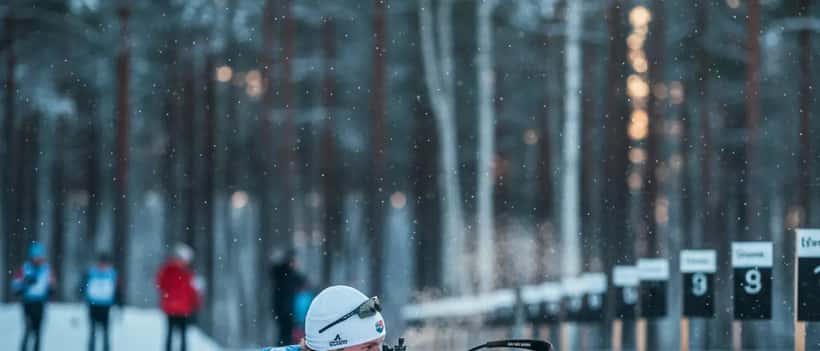 Nordisk skidskyttare i skjutposition i snöigt landskap under tävling