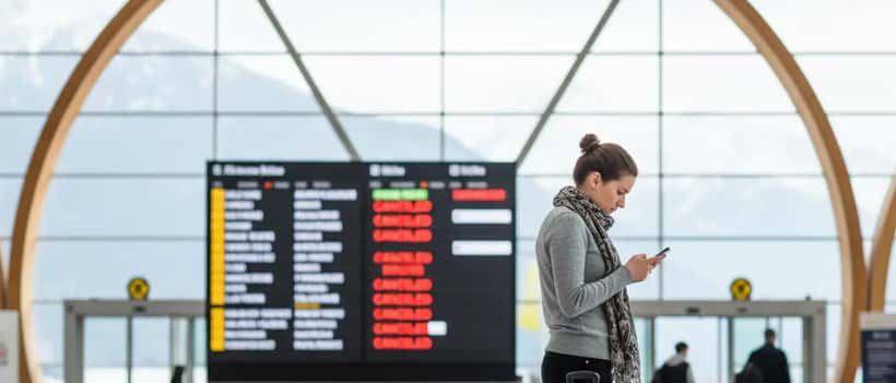 Österreichischer Reisender am Flughafen überprüft sein Smartphone wegen Flugstreichung mit Gepäck neben sich