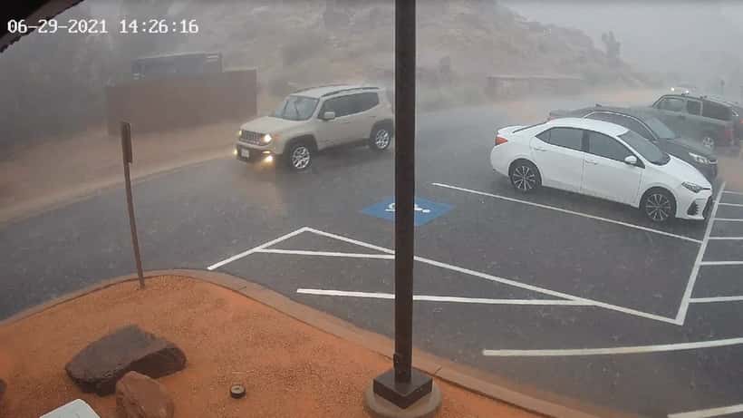 Hvid bil kører gennem kraftigt regn på en vej