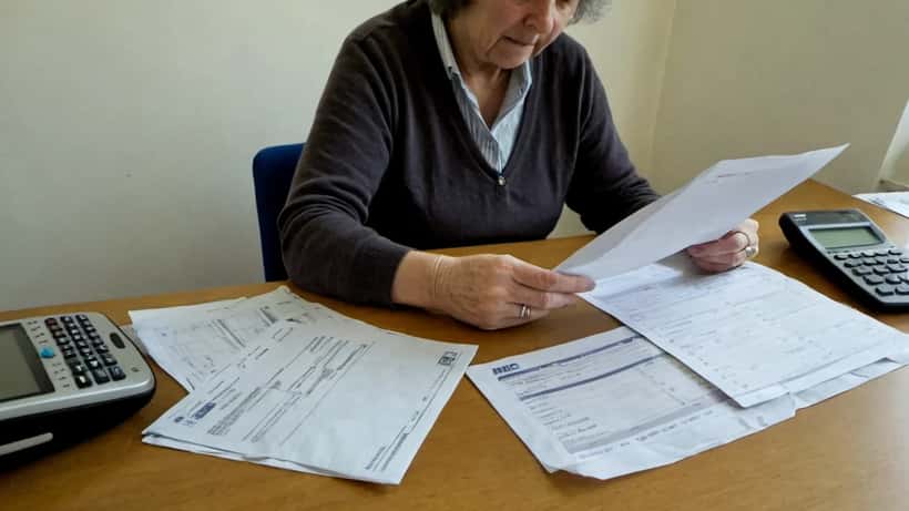 British woman reading an HMRC tax letter at a kitchen table with calculator and phone showing the HMRC app