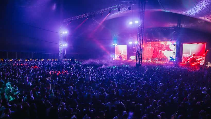 Festival crowd illuminated by stage lights at night concert representing hearing health risk from loud music
