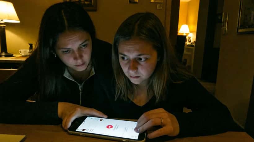Nederlandse moeder en tienerdochter aan keukentafel, kind scrollt op smartphone met sociale media apps