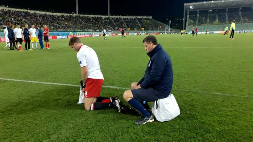 Fisioterapeuta examinando jogador de futebol lesionado na beira do campo durante partida da Serie A italiana