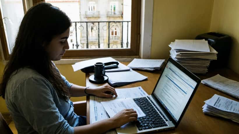 Jovem portuguesa a rever declaração de IRS no computador com documentos fiscais em cima da mesa