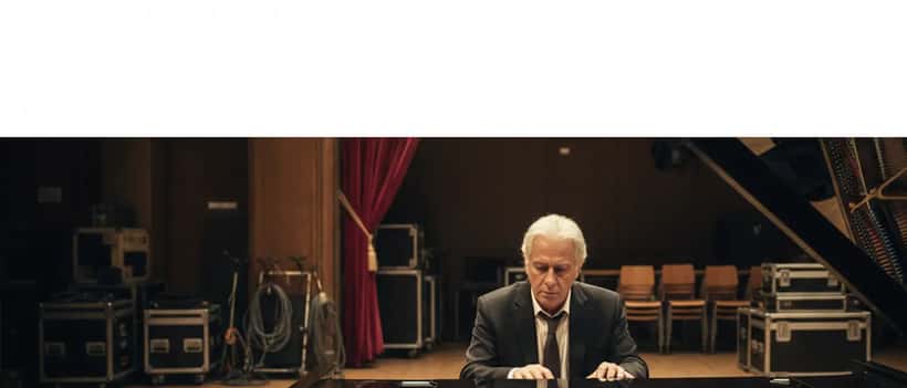 Musicista italiano di mezza età seduto pensieroso al pianoforte backstage