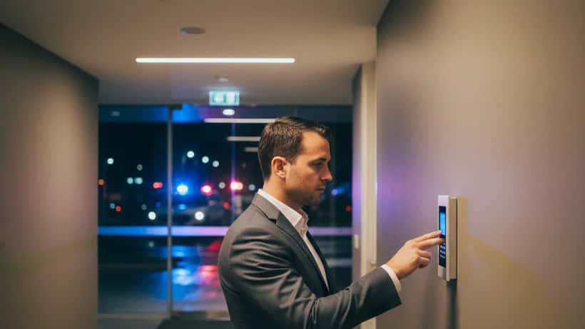 Security expert checking access panel in Melbourne high-rise apartment building at night with police lights
