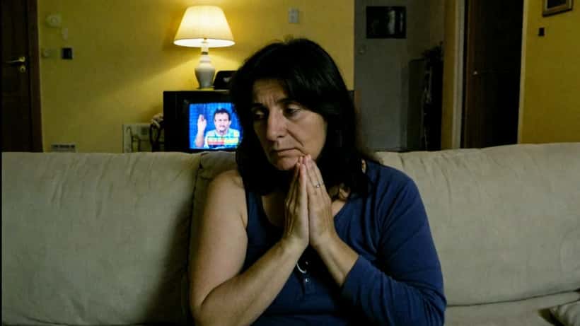 Coppia italiana che guarda Affari Tuoi in televisione con evidente tensione e ansia
