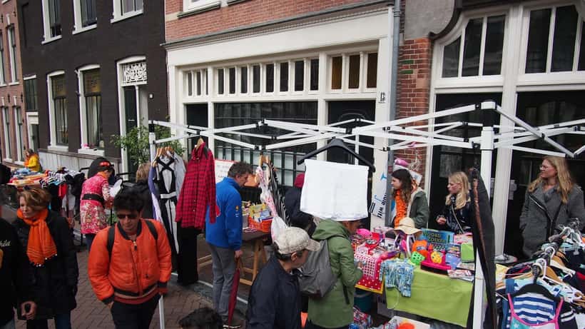 Drukke gracht in Amsterdam vol met feestende mensen in oranje kleding tijdens Koningsdag, boten en vrijmarkt op de wal