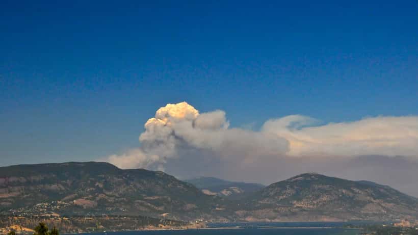 Forest fire burning over a lake in BC's southern interior, smoke filling the sky