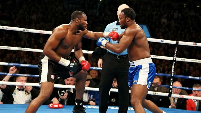 A referee raises his arm between two heavyweight boxers inside a professional boxing ring