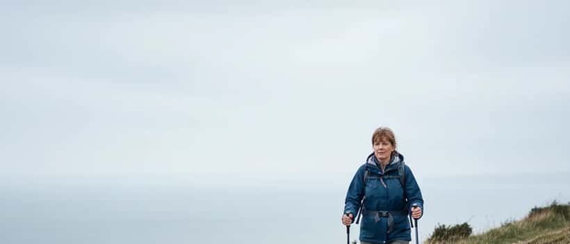 Woman hiking along rugged British coastal path representing nature therapy and chronic illness resilience