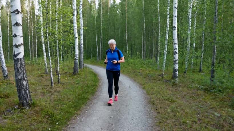 Nainen kävelee rivakasti suomalaisessa metsässä ja tarkistaa älykelloa