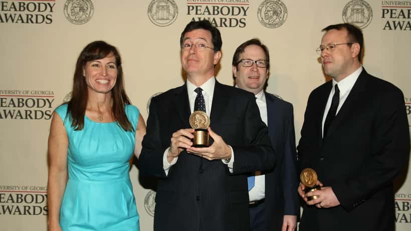Stephen Colbert lors d'une cérémonie de remise de prix, regard expressif, micro en main