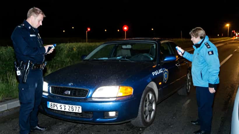 Politibetjent stopper bil på motorvej om natten, blinkende politilys på vådt asfalt