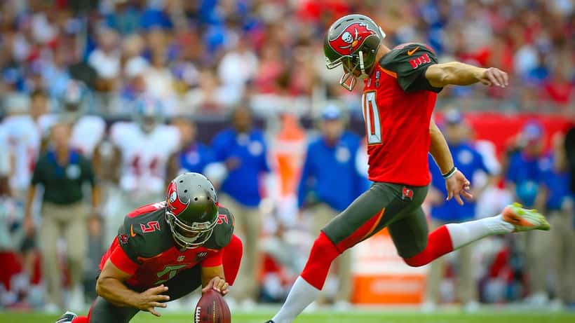 NFL player attempting a field goal during game action with crowd in background