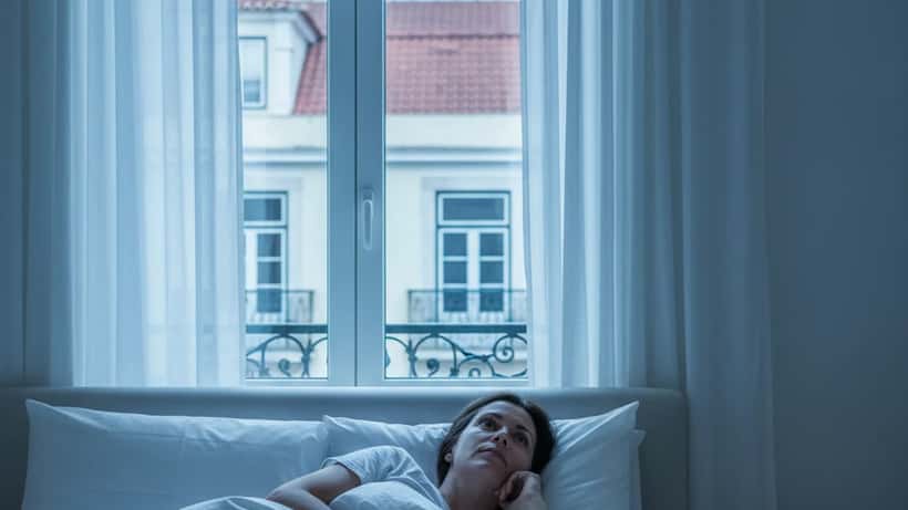 Mulher acordada de madrugada com luar entrando pela janela em Lisboa — efeitos da lua cheia no sono