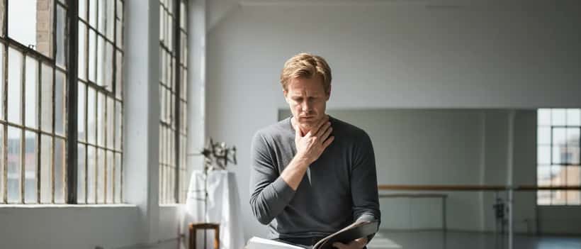 Actor rehearsing in a studio with hand on throat, voice coaching session