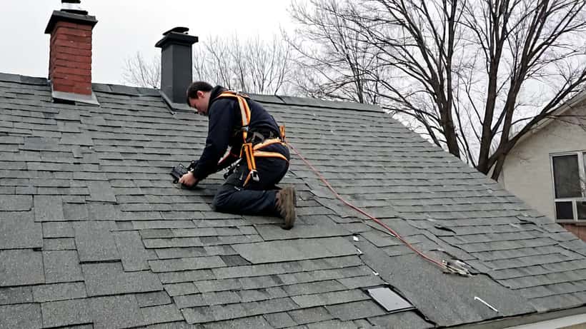 Couvreur inspectant les bardeaux d'une maison québécoise après les tempêtes printanières