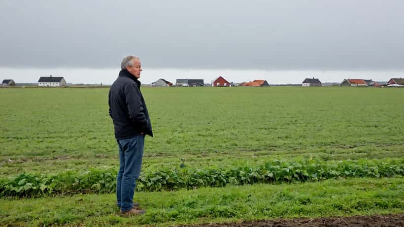 Dansk landmand alene på en mark i Jylland med overskyet himmel — symboliserer rural ensomhed