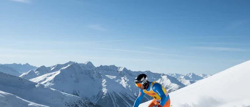 Professioneller Skifahrer auf steiler österreichischer Piste im Sonnenschein, Alpen im Hintergrund