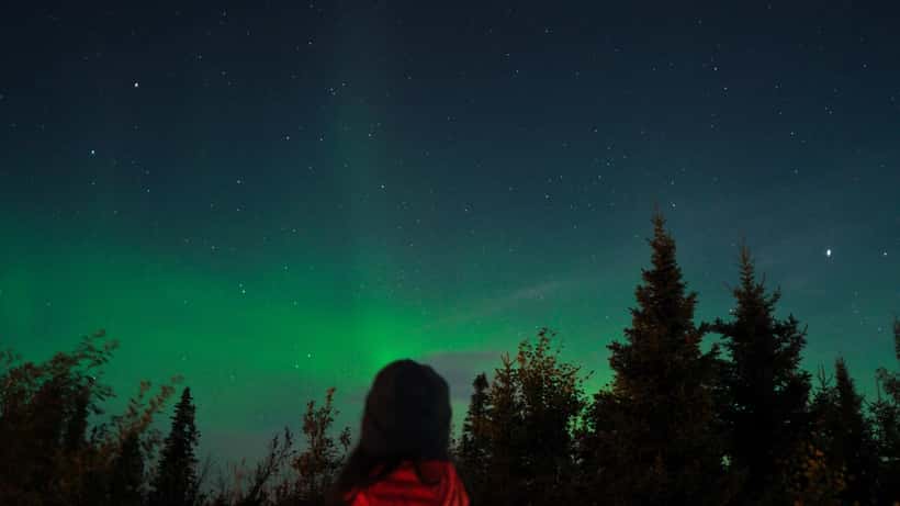Woman watching the aurora borealis illuminate the night sky over Chisasibi, Quebec, Canada